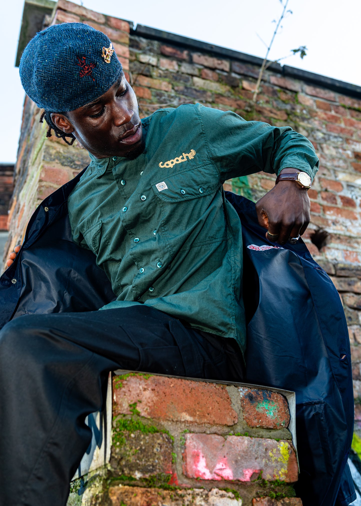 Man wearing Apache Tribe Belfast 2 Button Green Shirt with gold Capache logo embroidery, styled with navy jacket and blue beret