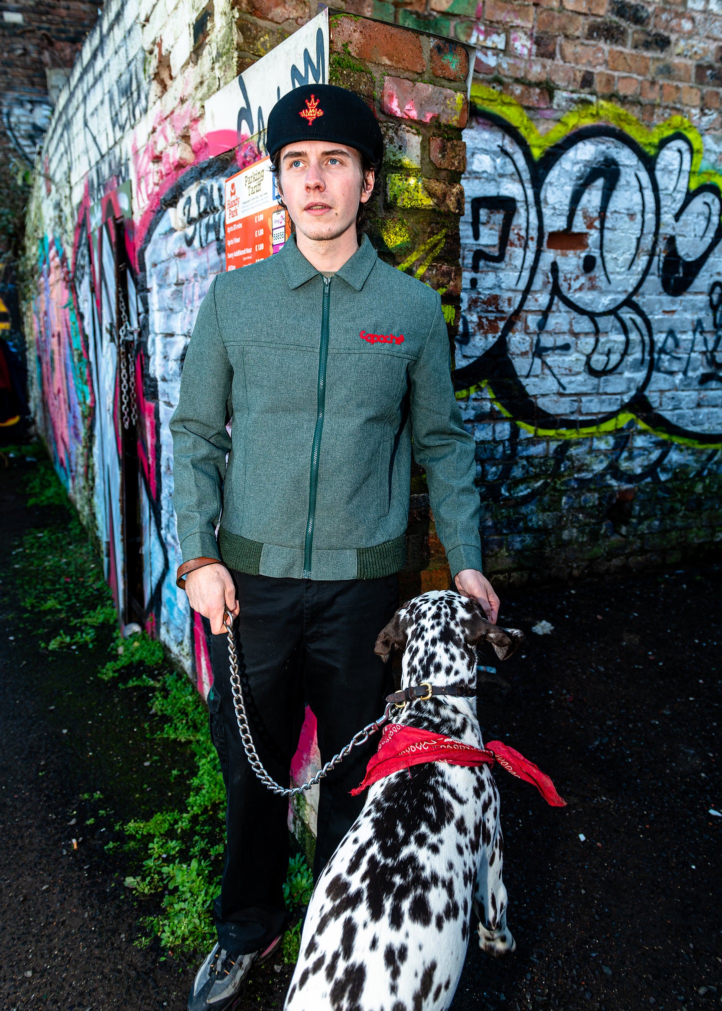 Man wearing Apache Tribe Belfast Mens Zip Jacket in sage green with red embroidered logo, styled with black beanie and trousers
