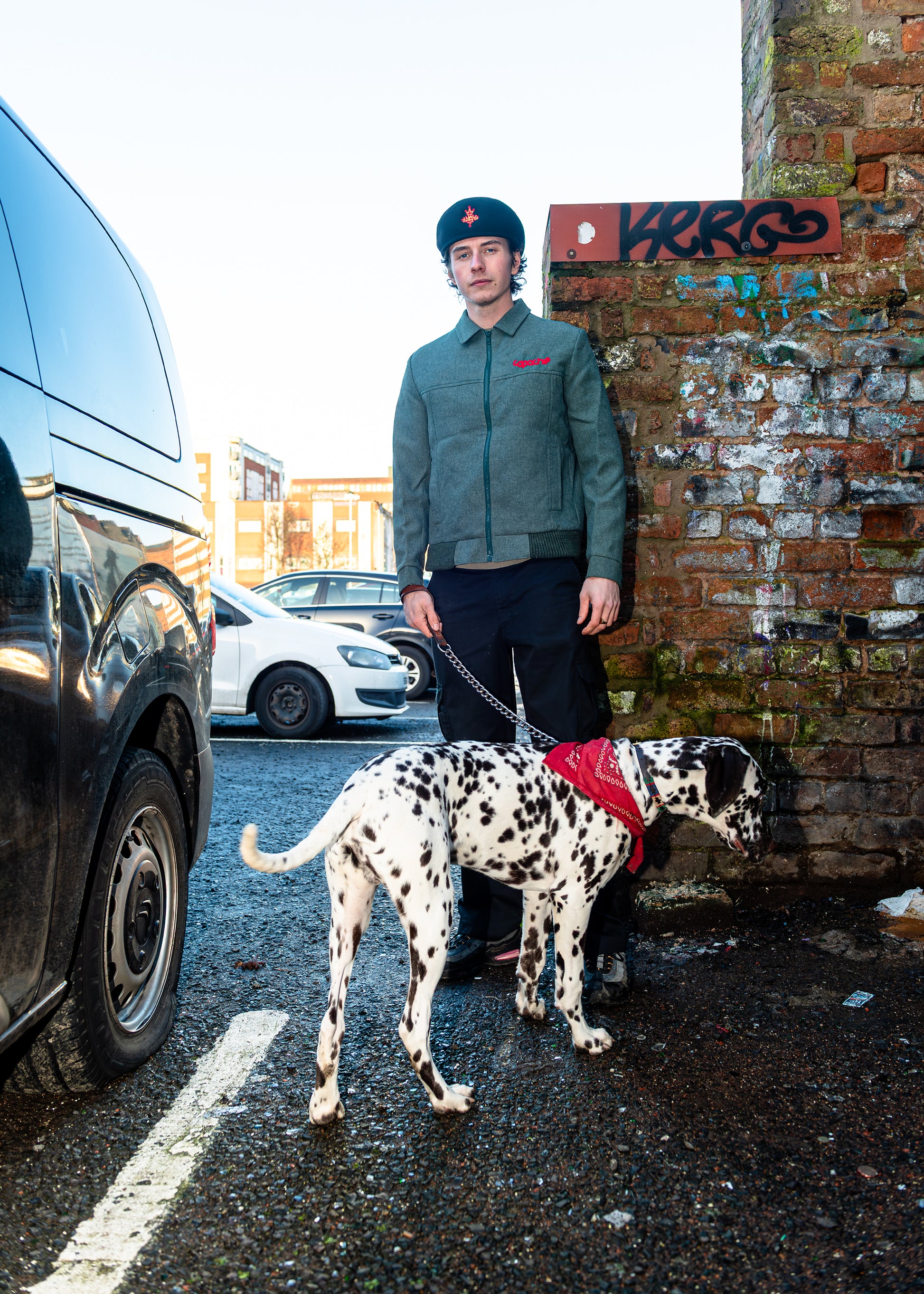 Man wearing Apache Tribe Belfast Mens Zip Jacket in grey with red logo embroidery, paired with black cargo pants and beret