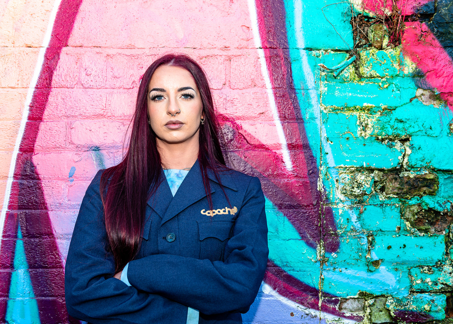 Woman wearing Blue Tailored Blazer Gold Apache navy structured jacket with gold Apache logo pin streetwear against colorful graffiti wall