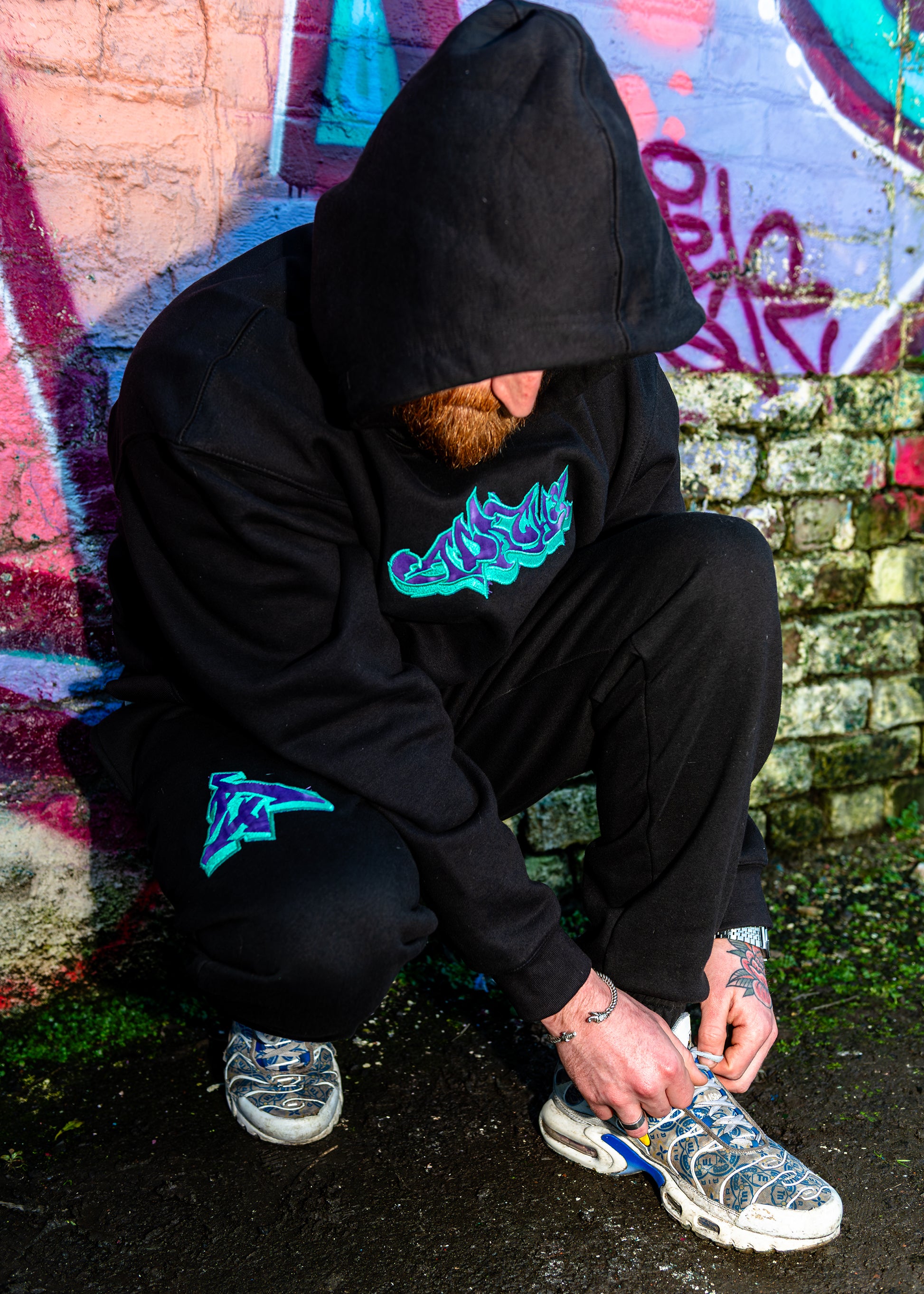 Black heavyweight hoodie and joggers set featuring purple and teal graffiti-style Joker appliqué design, Apache Tribe Belfast A logo on sleeve