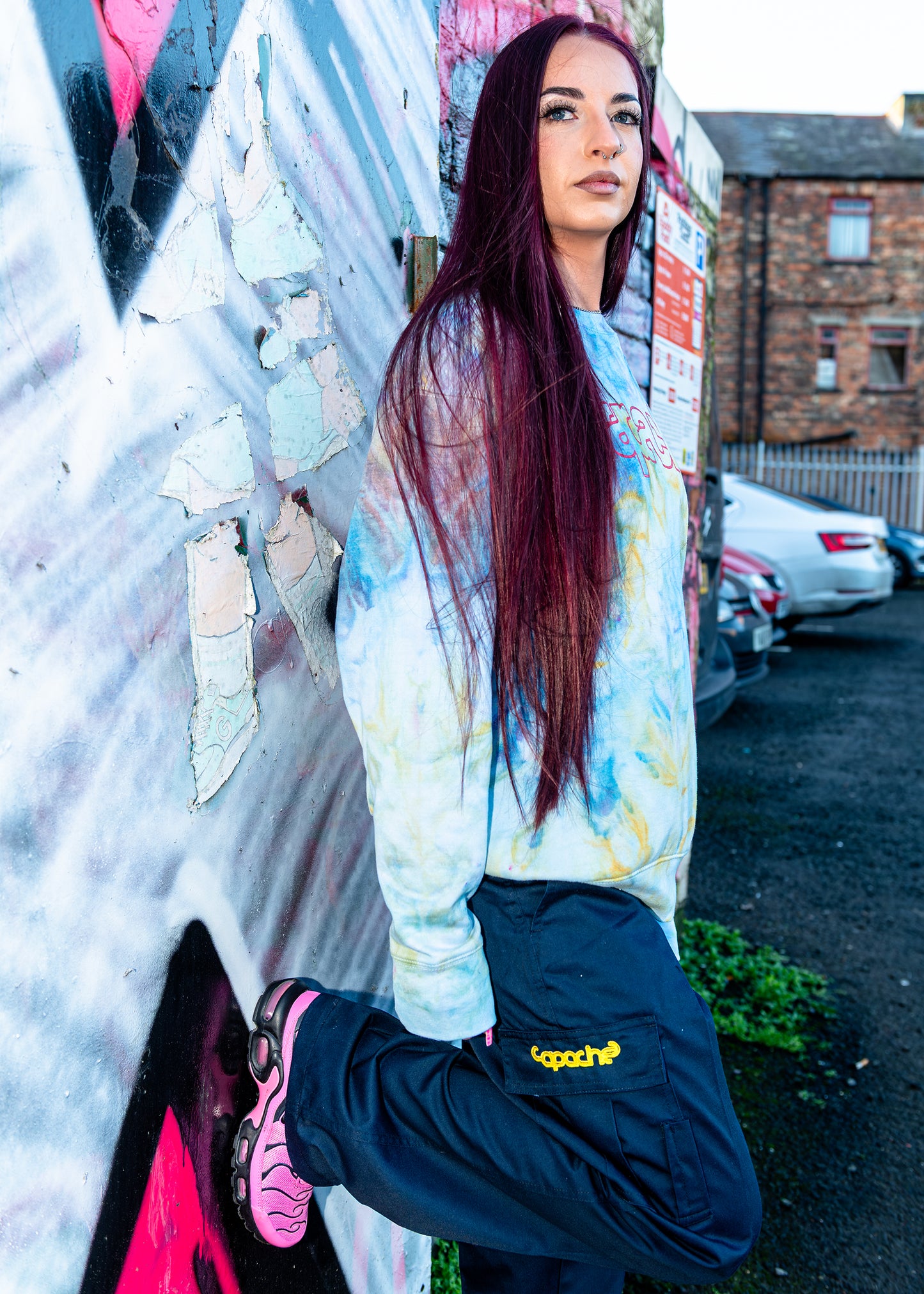 Woman wearing Apache Ice Dye Crewneck sweatshirt in pastel blue yellow and white tie-dye pattern with pink logo graphic