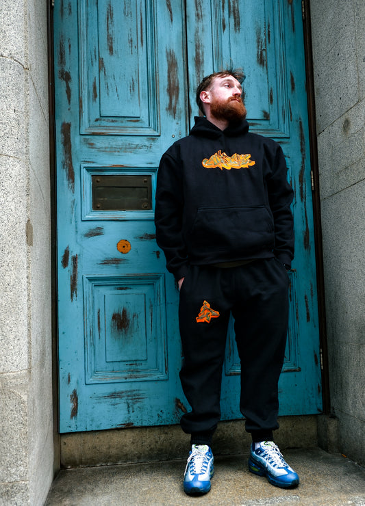 Man wearing Apache Charizard Appliqué Sweats in black featuring orange graffiti-style graphics on hoodie and joggers